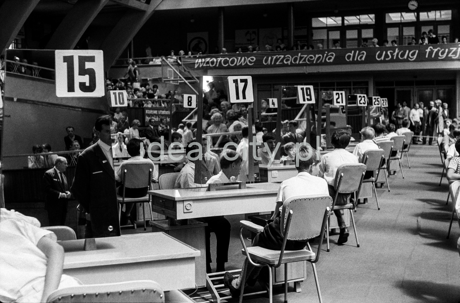 Boys in white shirts are sitting at two rows of tables with numbers.
