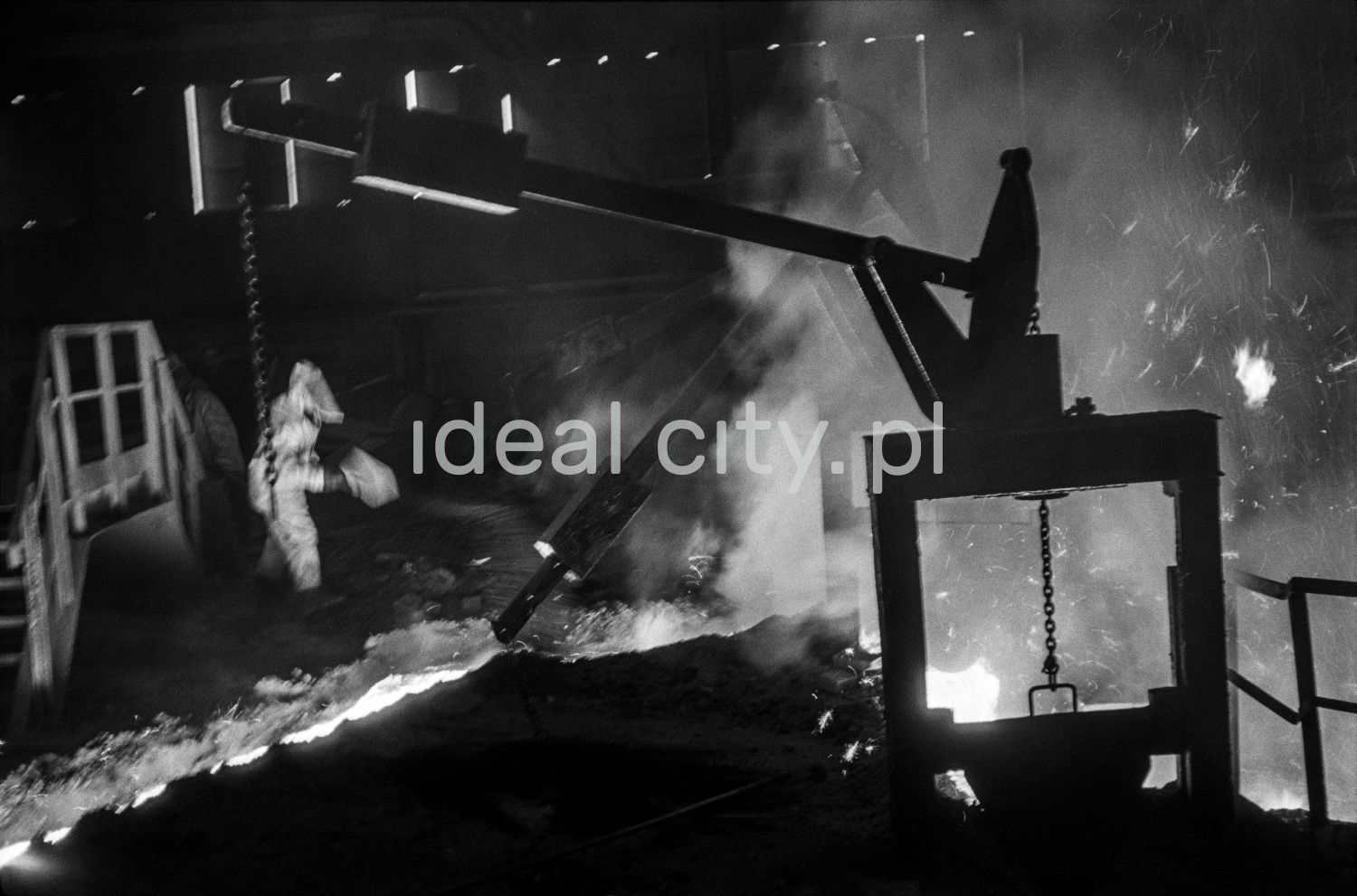 A steelworker in full outfit controls a stream of molten pig iron with a shovel.