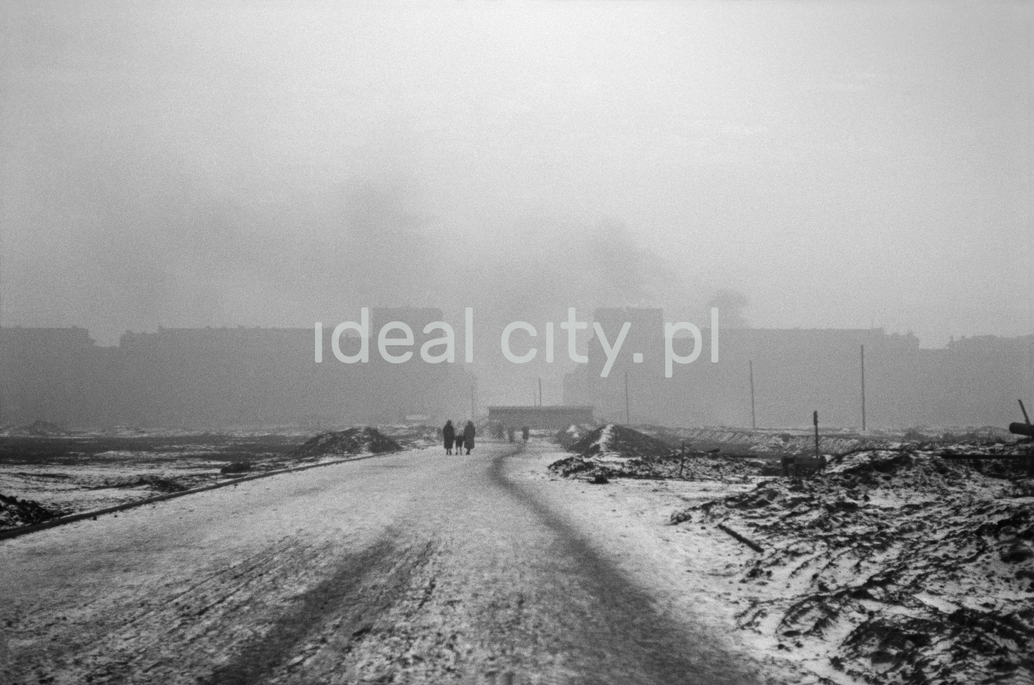 Central view of the frost-covered road and fields to the sides, outlines of massive apartment blocks in perspective.