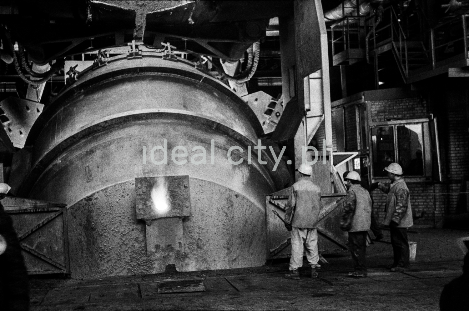 The steelworkers stand at the throat cover of the mighty furnace.
