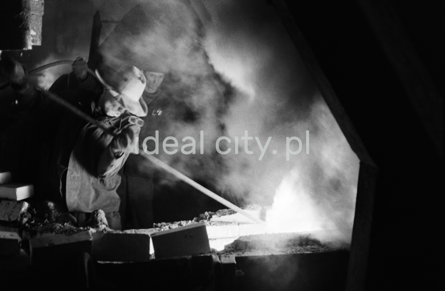 A steelworker in a costume turns a rod in a stream of flowing and smoking pig iron