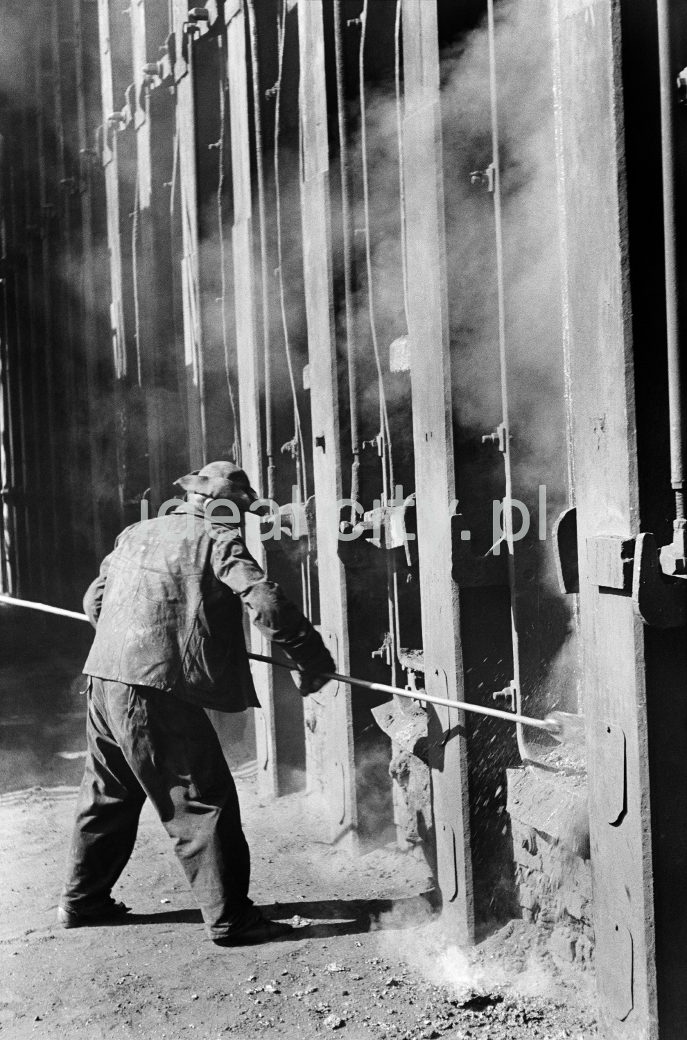 The steelworker inserts a long rod into a massive steel structure.