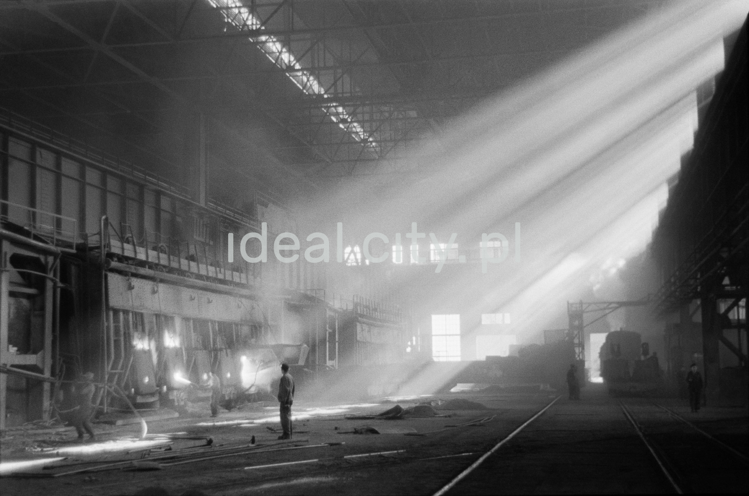 In the center of the hall, where the rays of the sun fall at an angle, there is a man in work clothes.