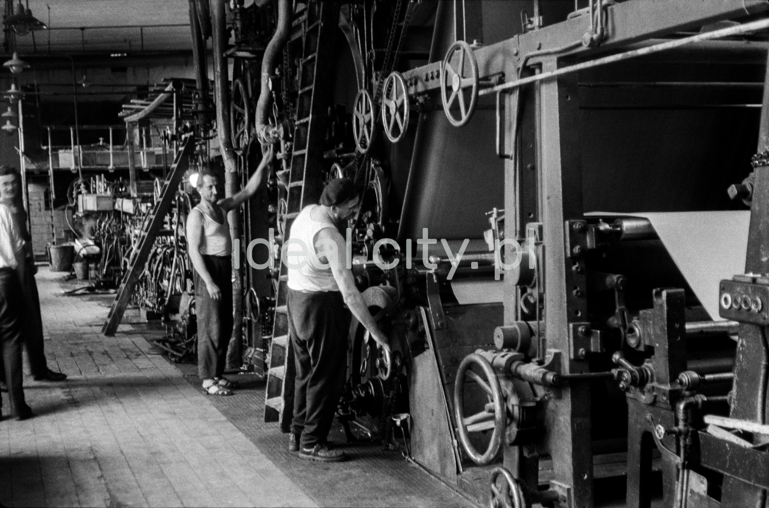Two men in tank tops regulate a powerful machine.