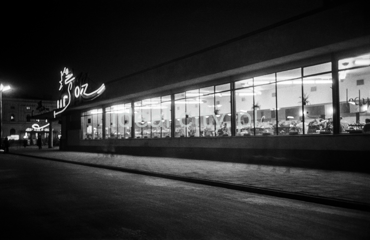 A night shot of a modernist lighted bar pavilion with a neon sign.