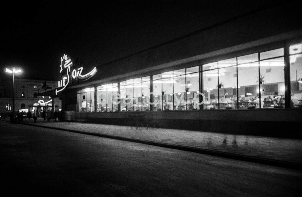 A night shot of a modernist lighted bar pavilion with a neon sign.