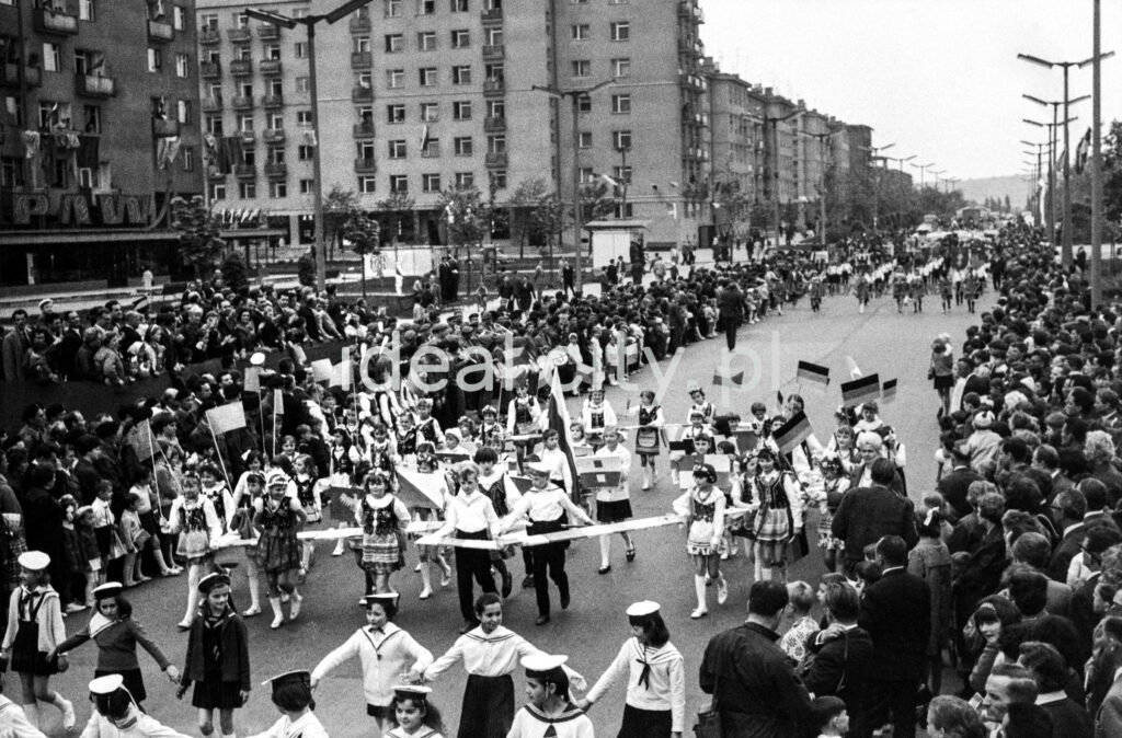 A view from the dais over a wide street where children are marching in a march, on the left a series of modernist blocks.