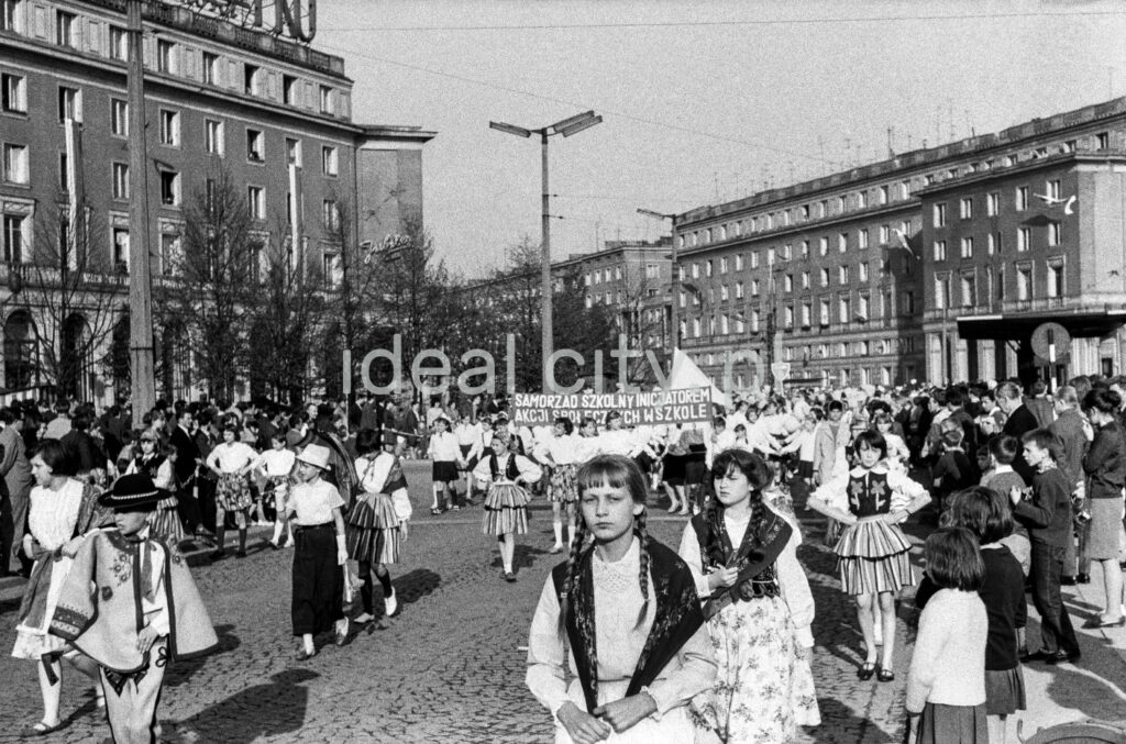 A view of the wide street where children are marching, with modernist apartment blocks in the background.