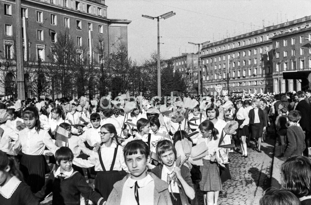 A view of the wide street where children are marching, with modernist apartment blocks in the background.