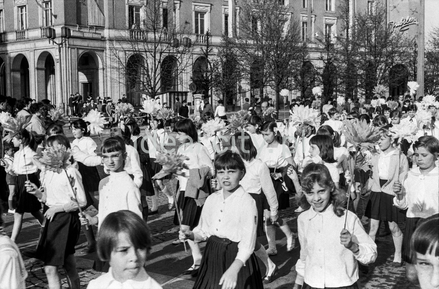 A view of the wide street where children are marching, with modernist apartment blocks in the background.