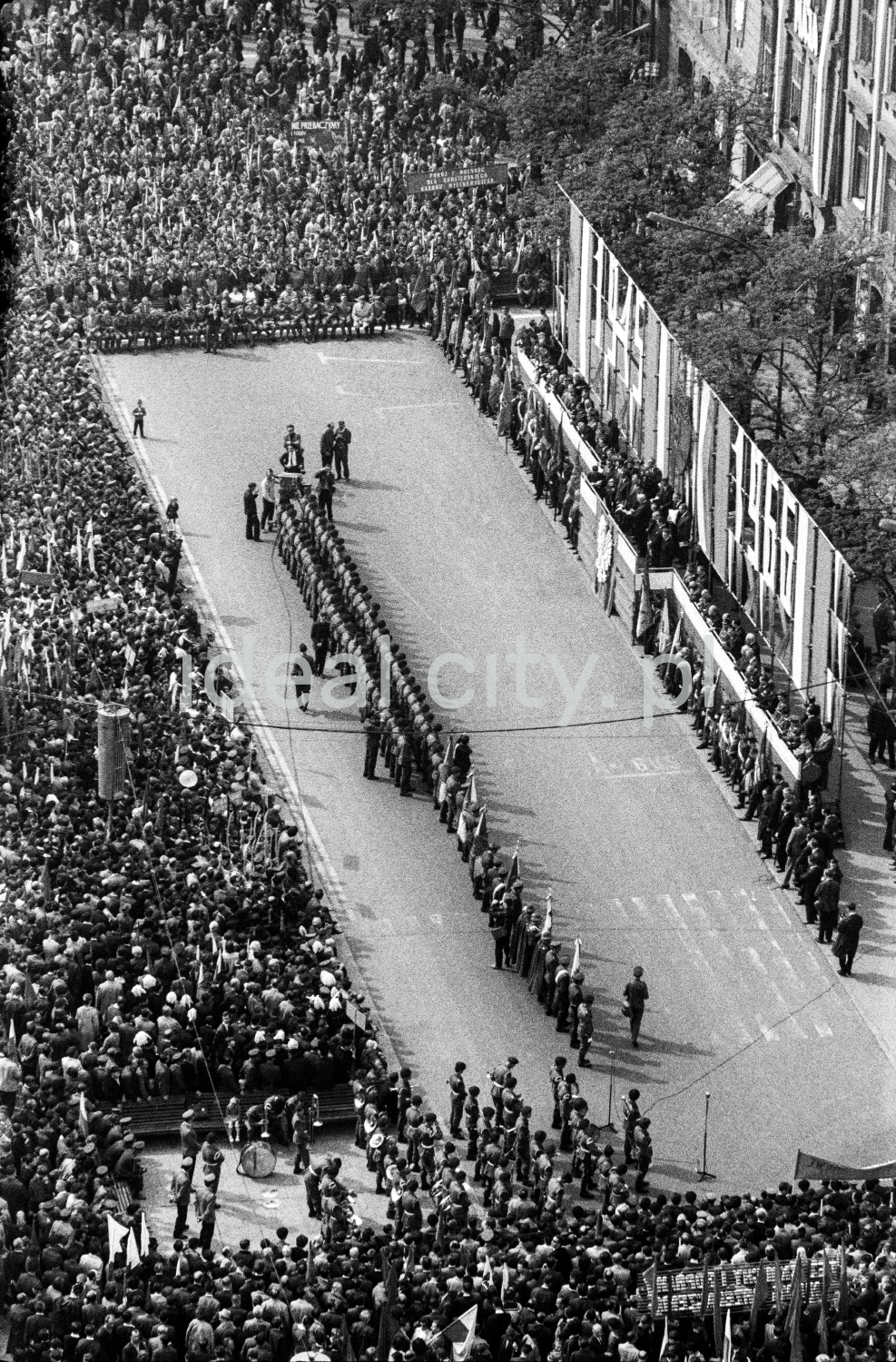 A view from above of the crowd gathered around the stage located in the town square surrounded by tenement houses