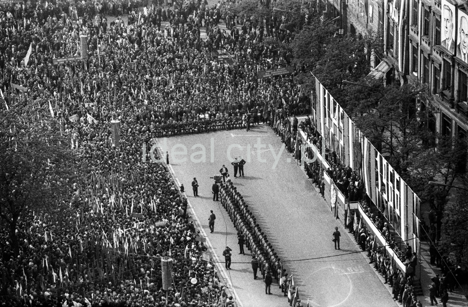 A view from above of the crowd gathered around the stage located in the town square surrounded by tenement houses