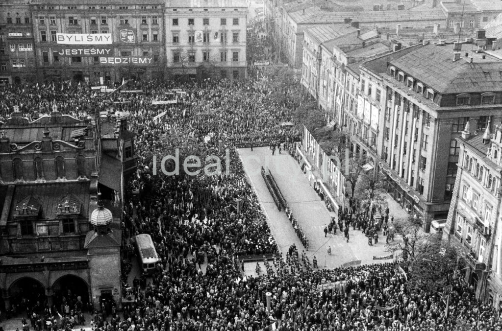 A view from above of the crowd gathered around the stage located in the town square surrounded by tenement houses
