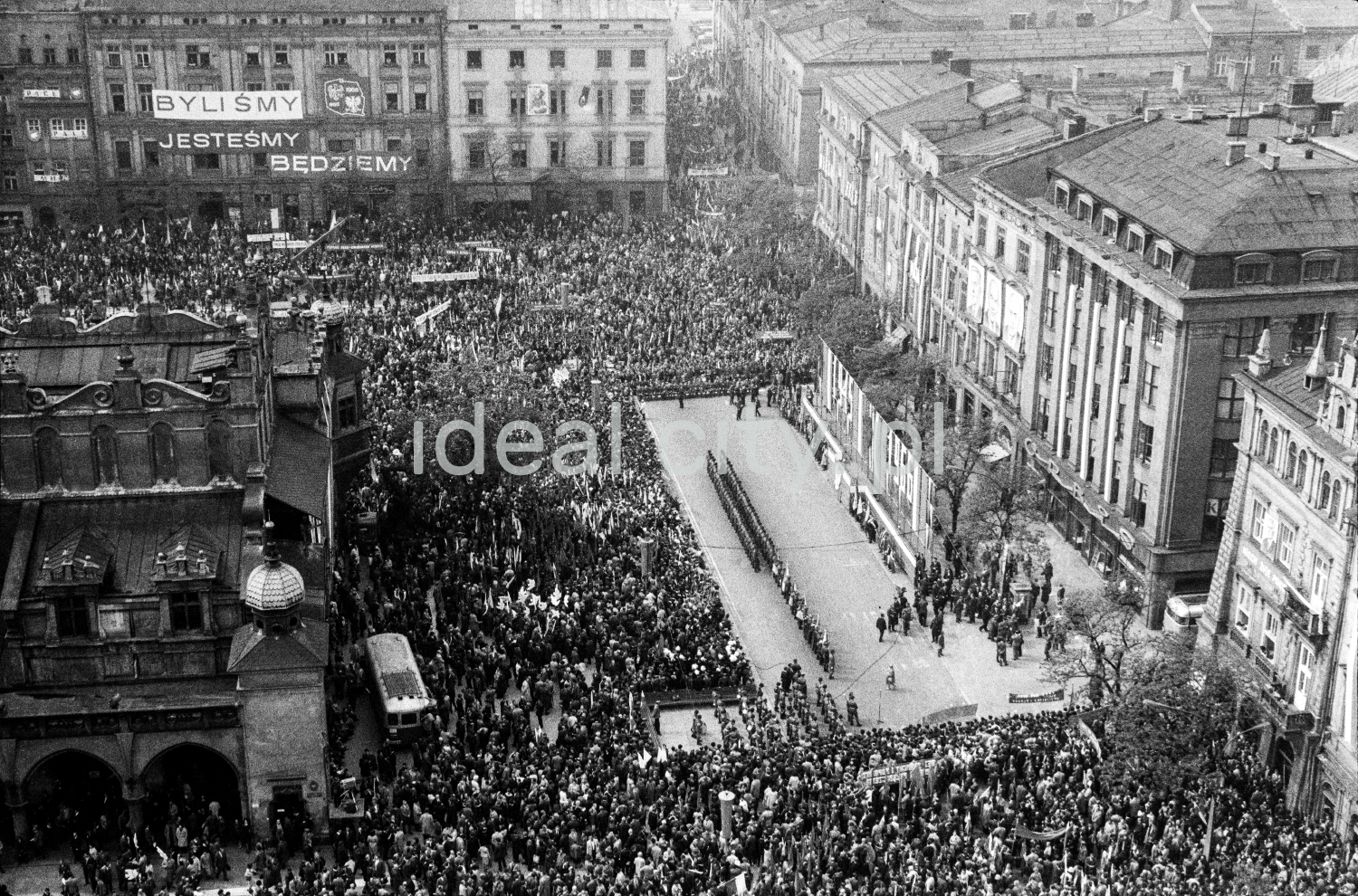 A view from above of the crowd gathered around the stage located in the town square surrounded by tenement houses