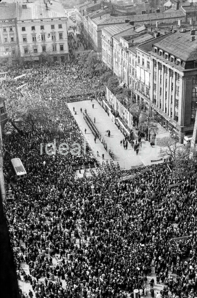 A view from above of the crowd gathered around the stage located in the town square surrounded by tenement houses