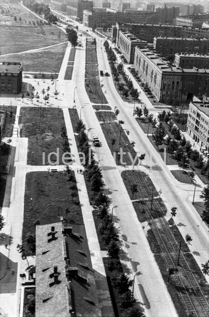 A bird's eye view of a wide avenue with a tram route in the middle, on the right a block of residential buildings.