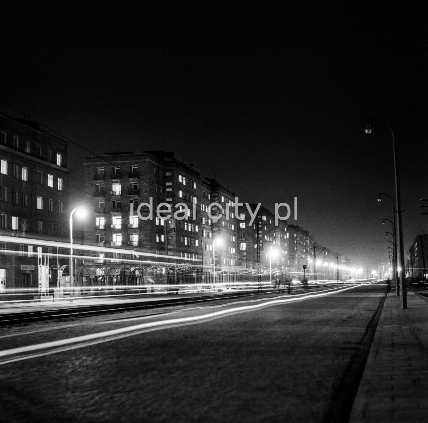Perspective of an illuminated, wide avenue with a tram route in the middle.