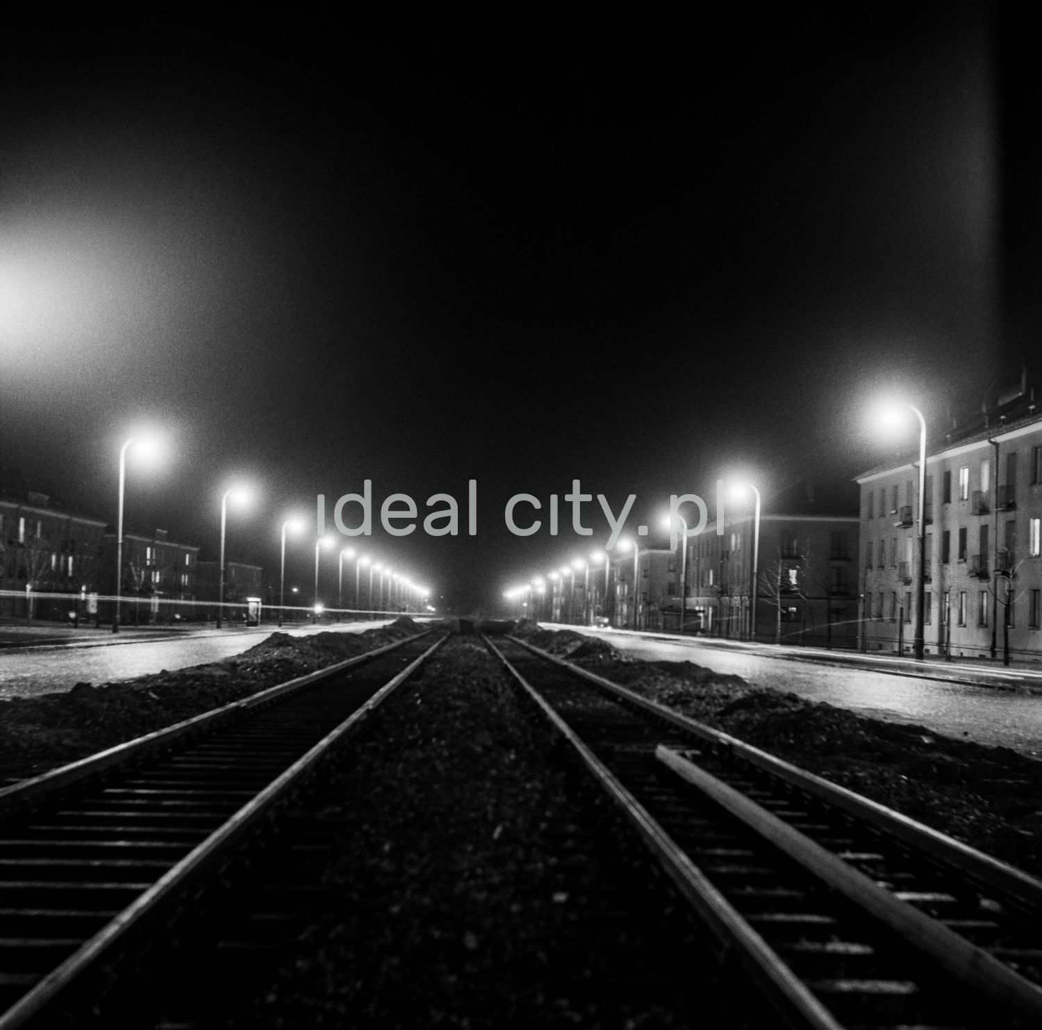 Central perspective of an illuminated, wide avenue with a tram route in the middle.