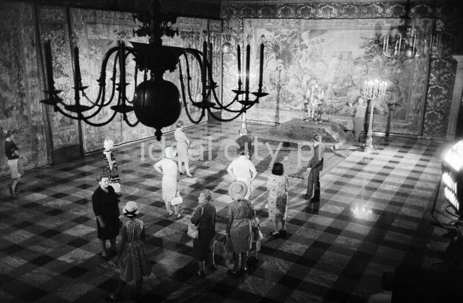 View from above on a group of tourists looking around the spacious room on the walls with tapestries.