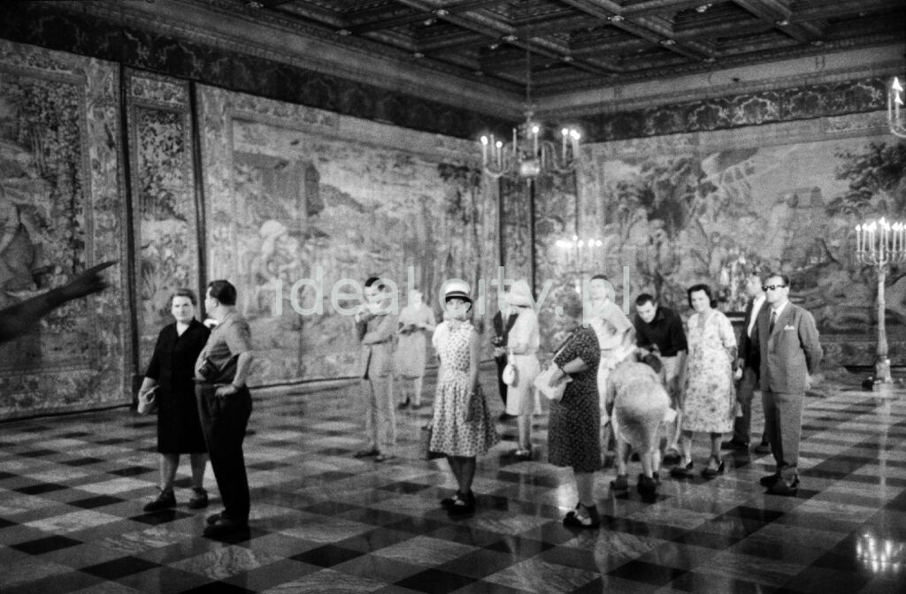 A group of tourists is looking around the spacious room on the walls with tapestries.