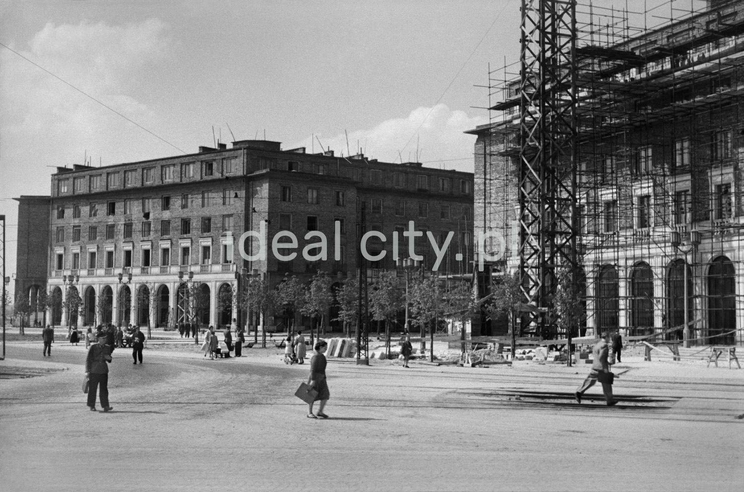 Pedestrian traffic on the spacious city square, monumental residential buildings under construction all around.