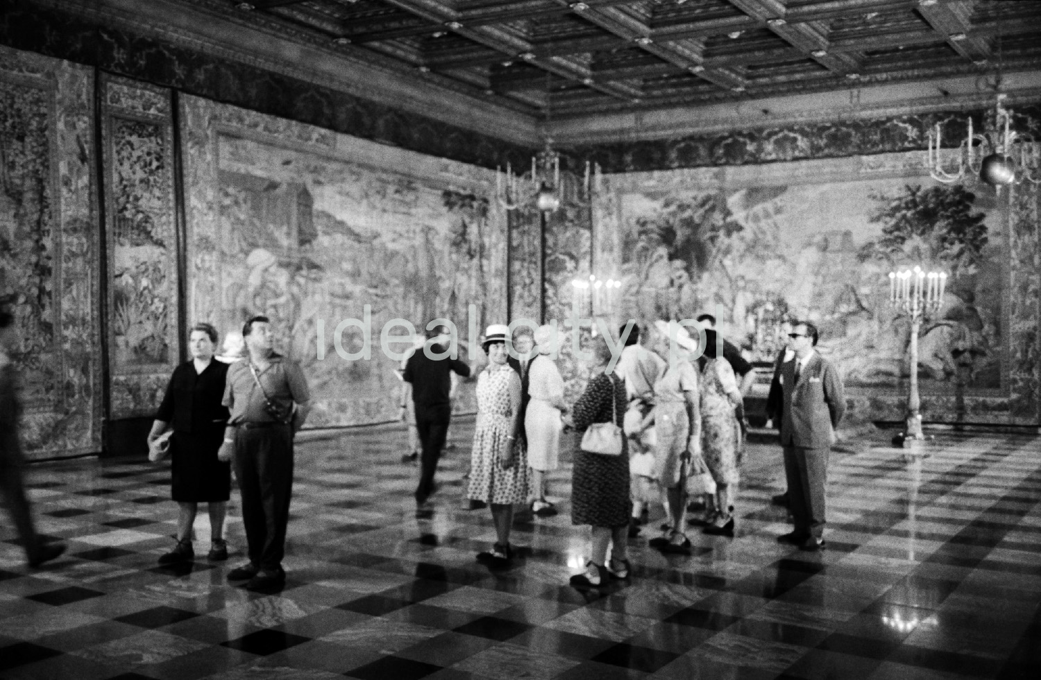 A group of tourists is looking around the spacious room on the walls with tapestries.