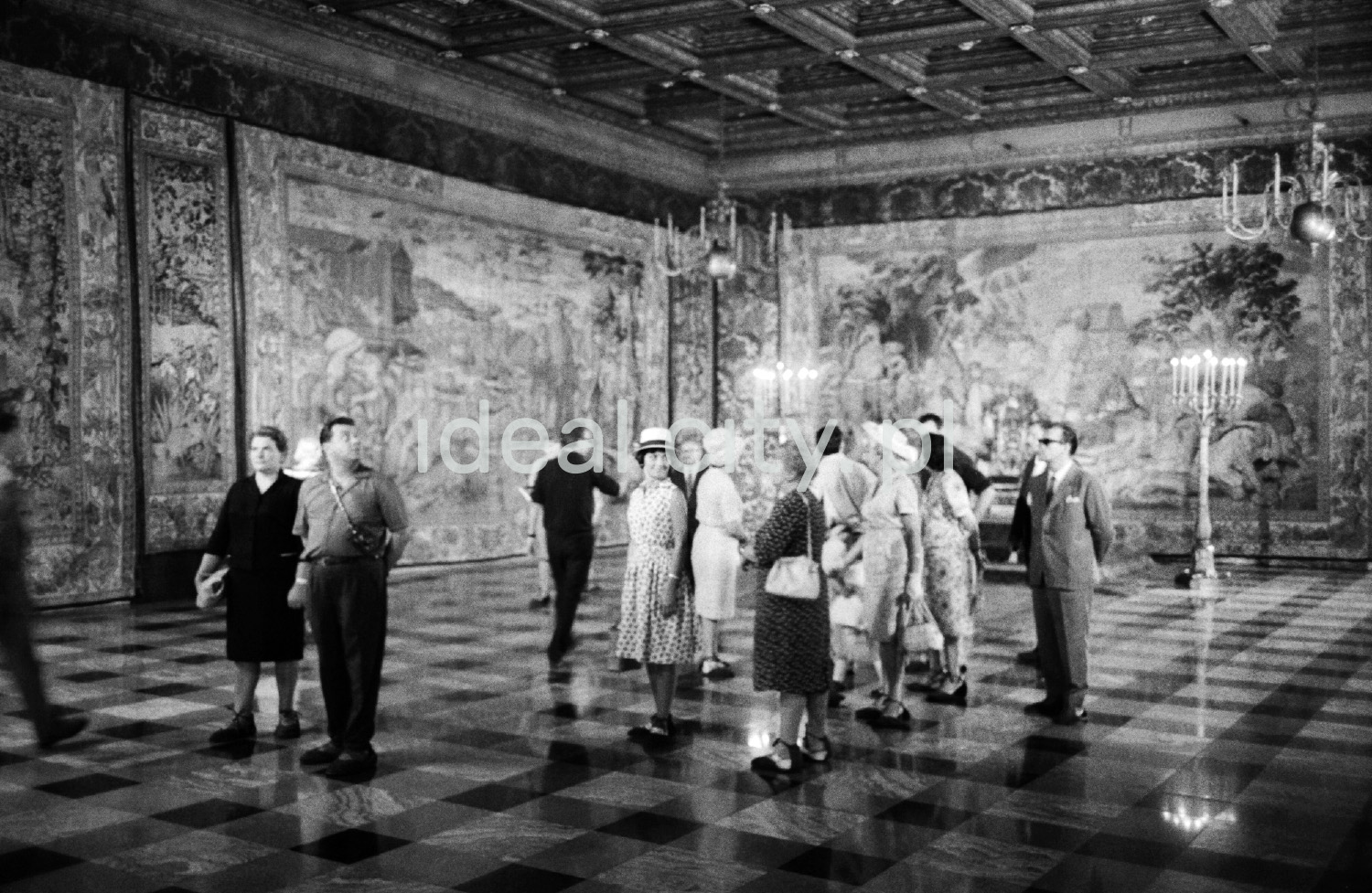 A group of tourists is looking around the spacious room on the walls with tapestries.