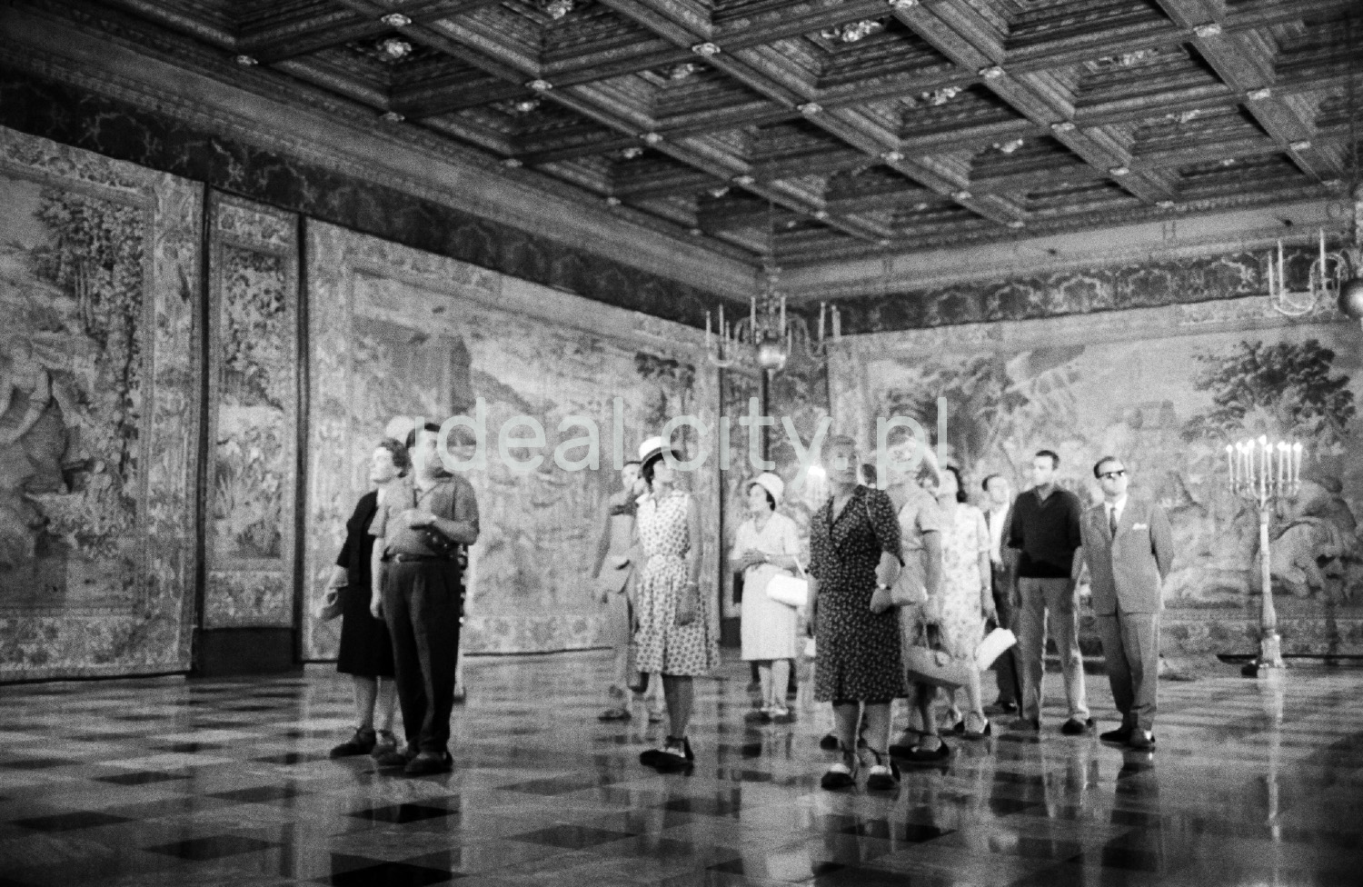 A group of tourists is looking around the spacious room on the walls with tapestries.