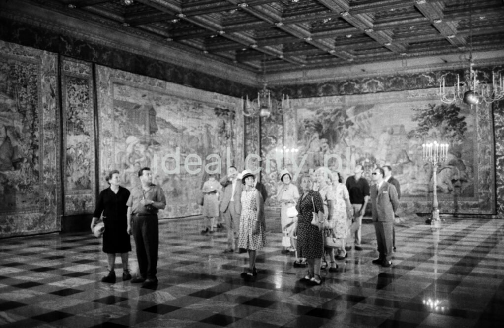 A group of tourists is looking around the spacious room on the walls with tapestries.