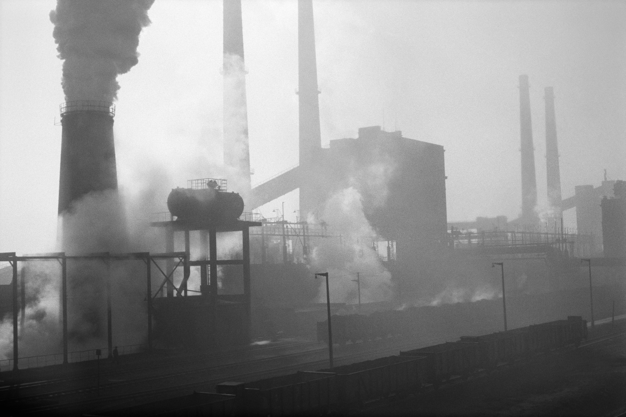 The shot shows a series of tall, intensely smoking chimneys.