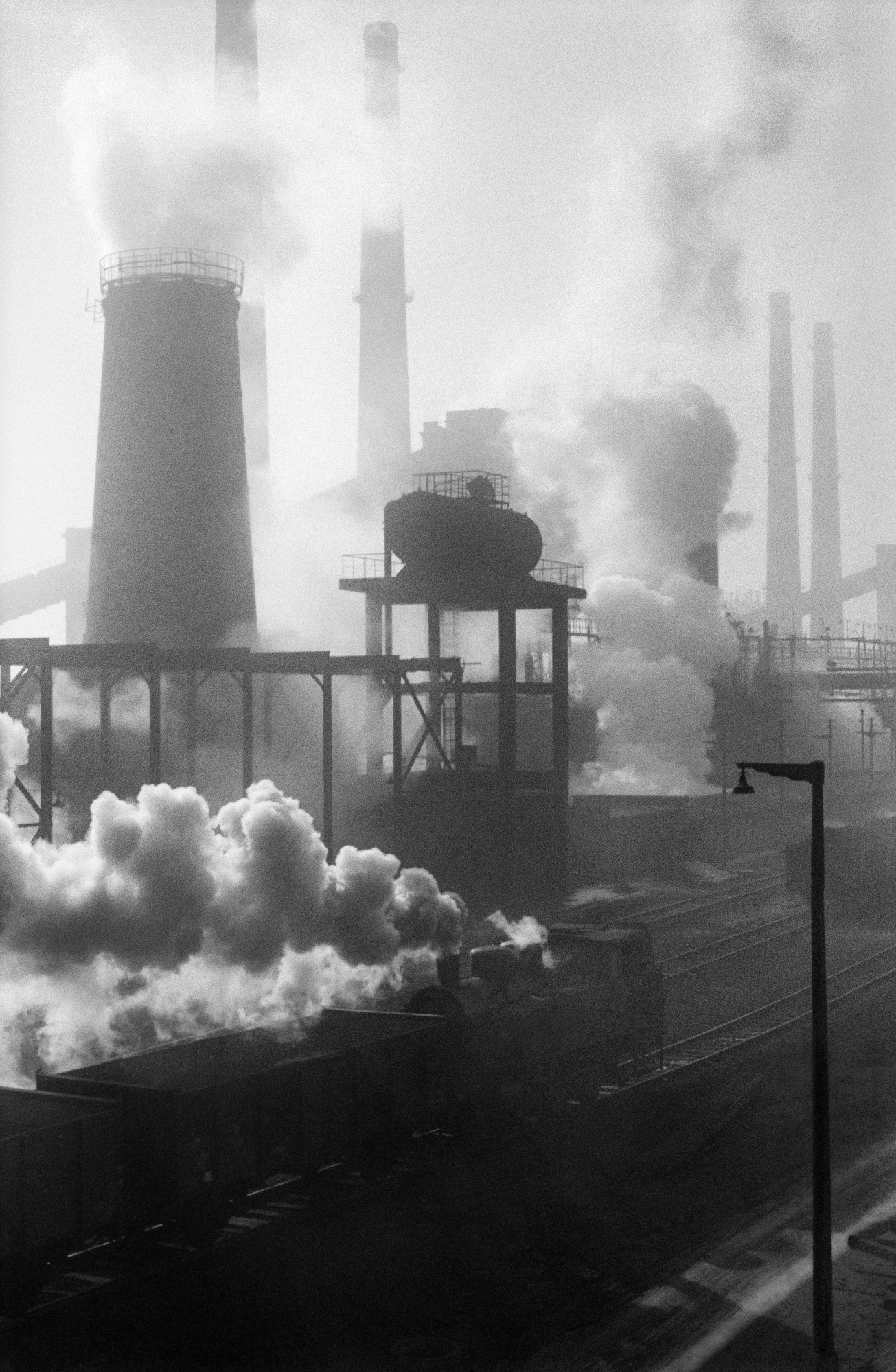 The shot shows a series of tall, intensely smoking chimneys.