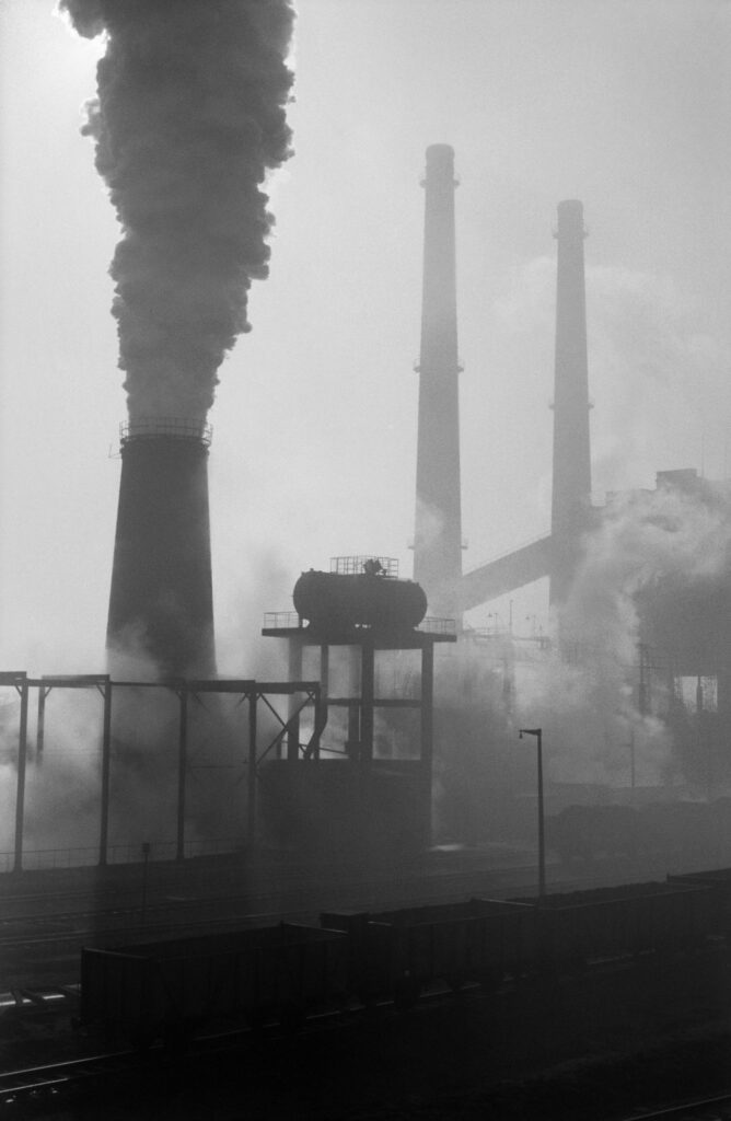 The shot shows a series of tall, intensely smoking chimneys.