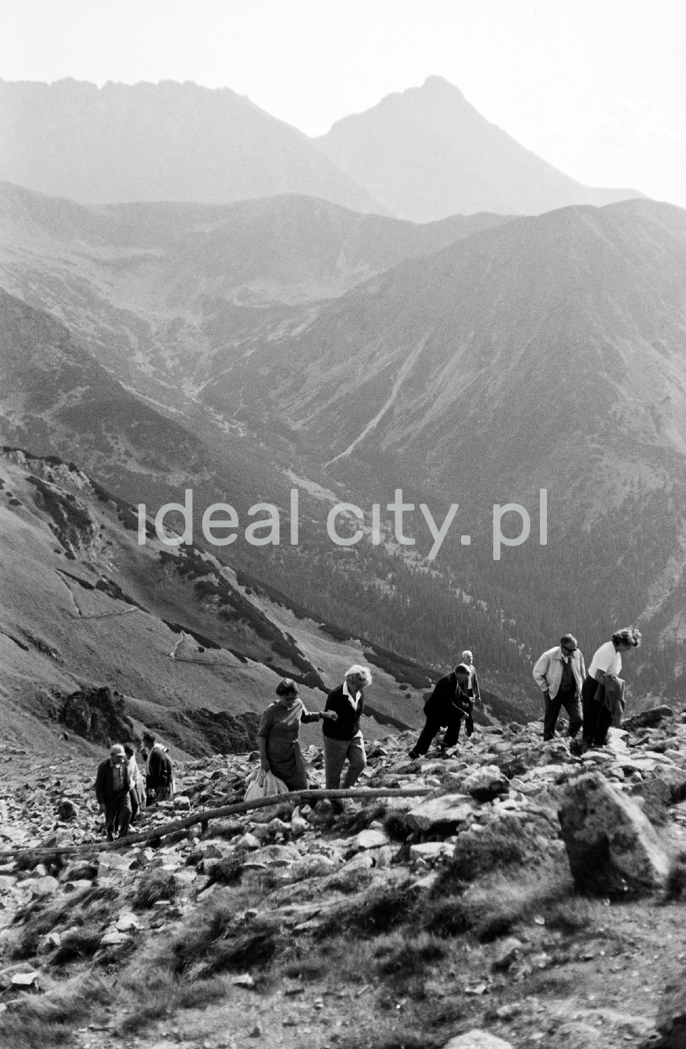 Tourists are walking along the rocky trail, with the perspective of the Tatra peaks in the background.
