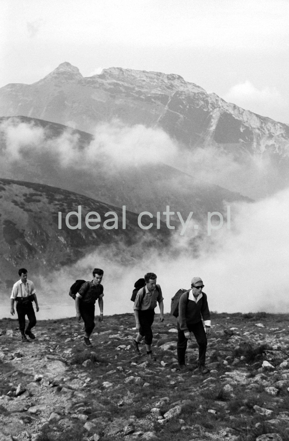 Tourists with backpacks are walking along the rocky trail, with the perspective of the Tatra peaks in the background.