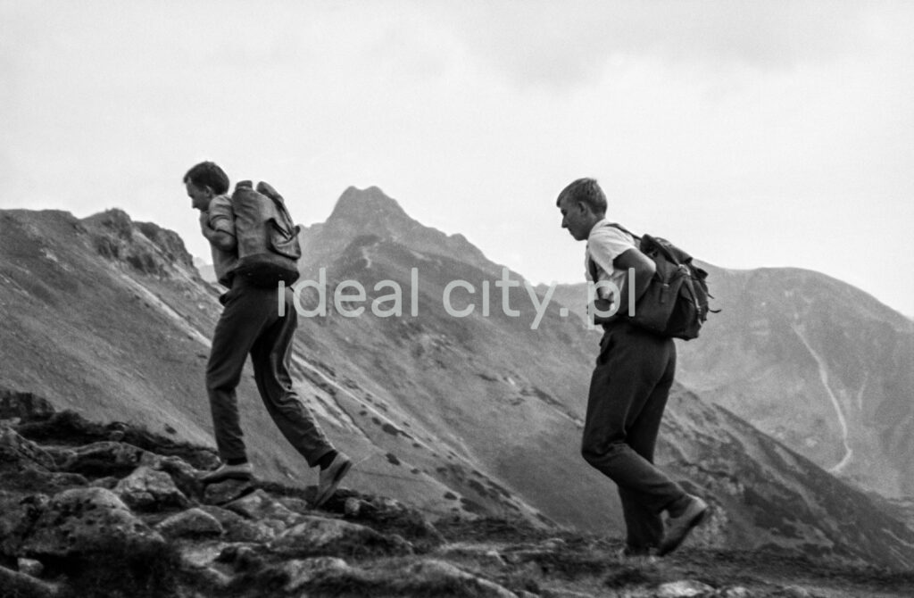 Tourists with backpacks are walking along the rocky trail, with the perspective of the Tatra peaks in the background.