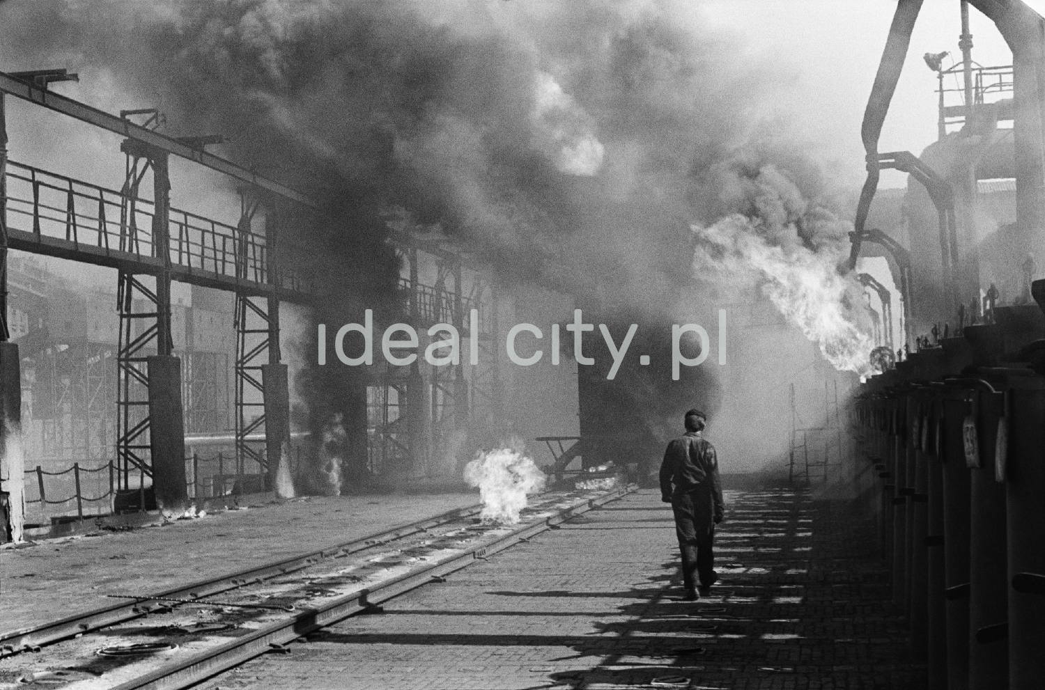 A man in workwear marches along the smoking installations of the coking plant.