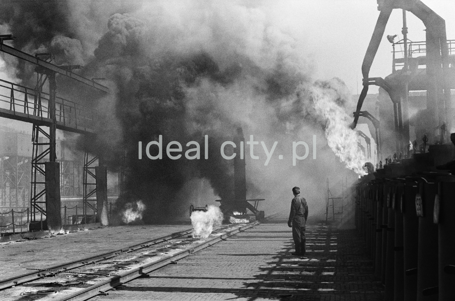 A man in workwear stands in the middle of the smoking installations of the coking plant.