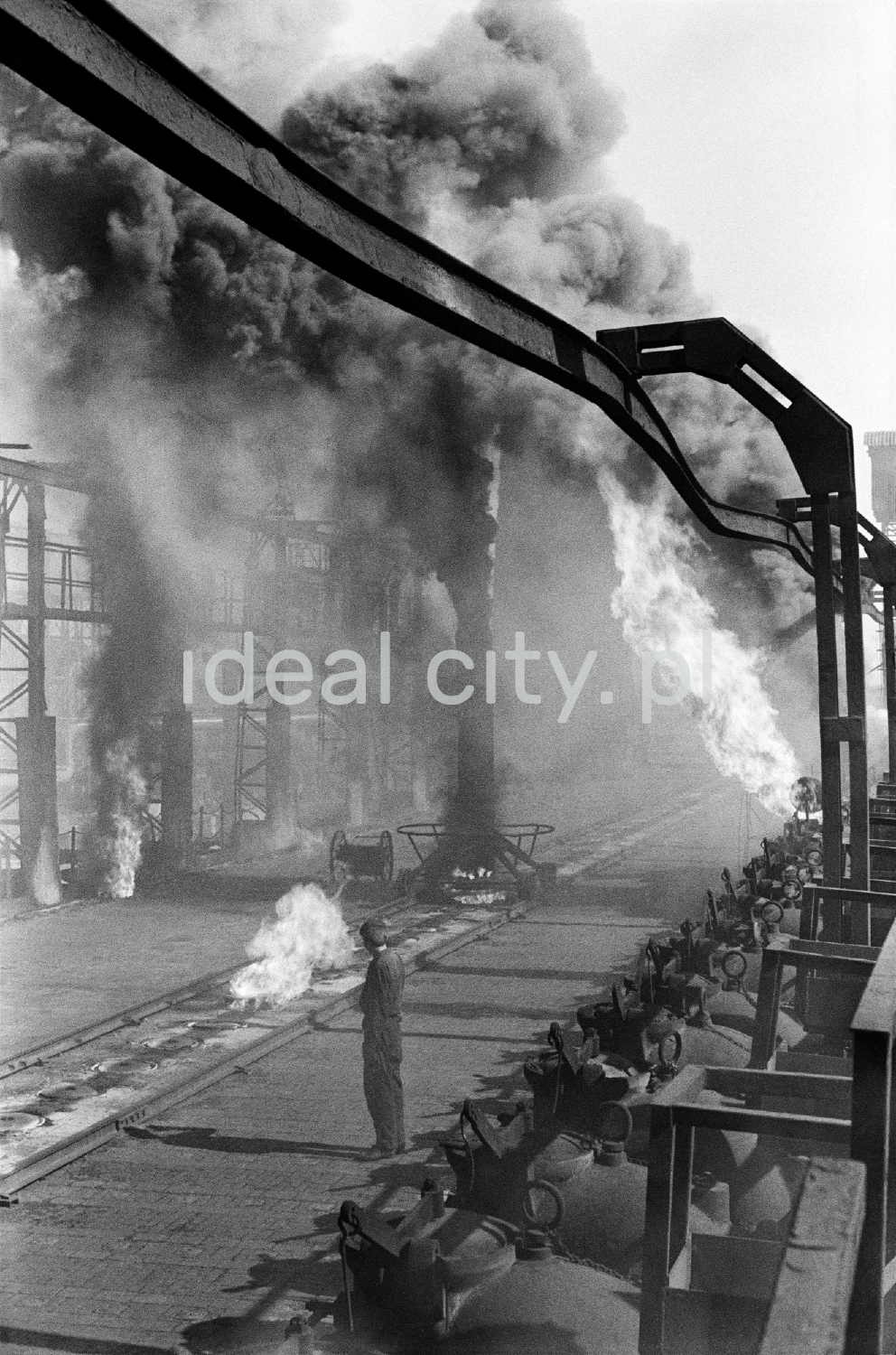 A man in workwear stands in the middle of the smoking installations of the coking plant.