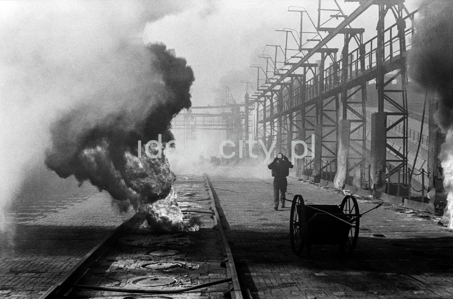 A man in denim walks through the middle of the smoking coking plant.