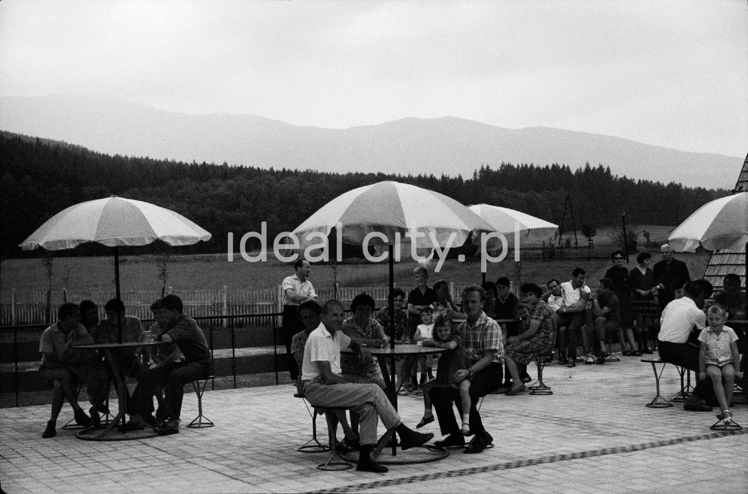 Holidaymakers sit at tables covered with umbrellas on the terrace of the holiday home.