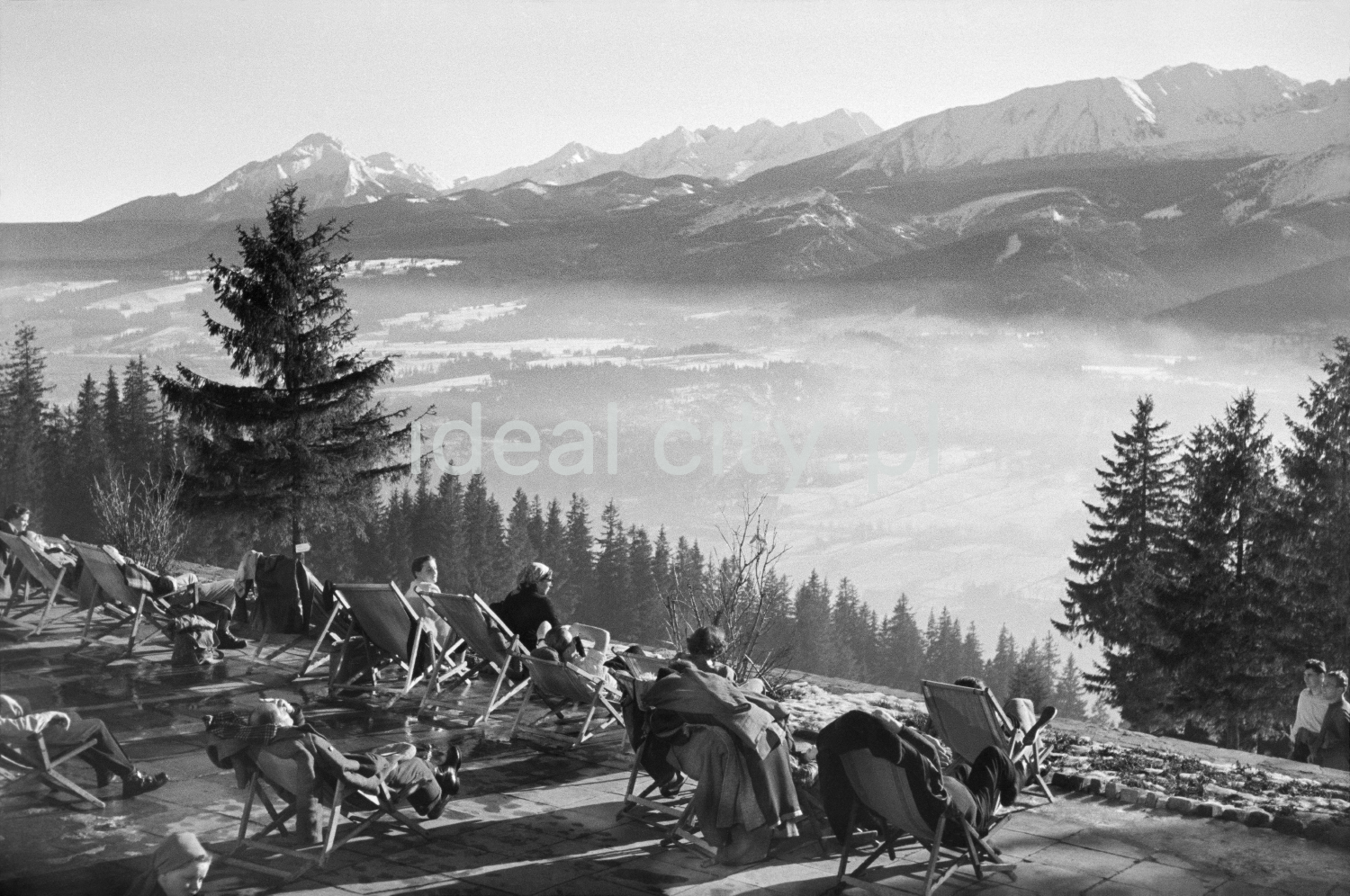 Winter patients relax in the sun on deckchairs at the top of the hill, in the background a panorama of mountain peaks.