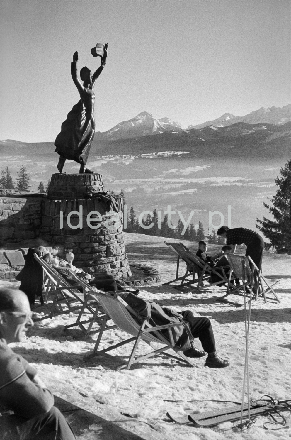 Winter patients relax in the sun on deckchairs at the top of the hill, in the background a panorama of mountain peaks.