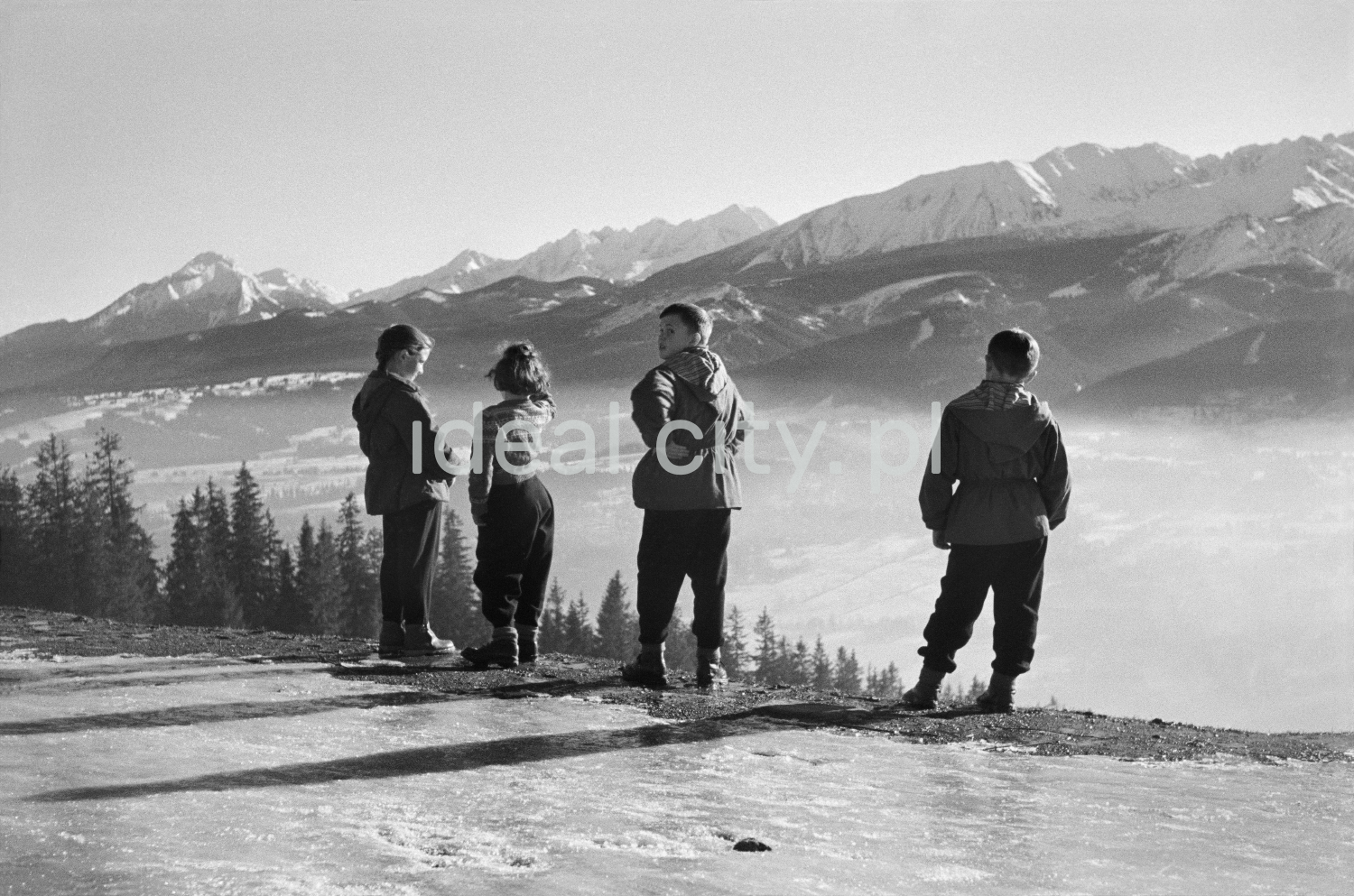 Young people watch the winter panorama of mountain peaks from the top of the hill.