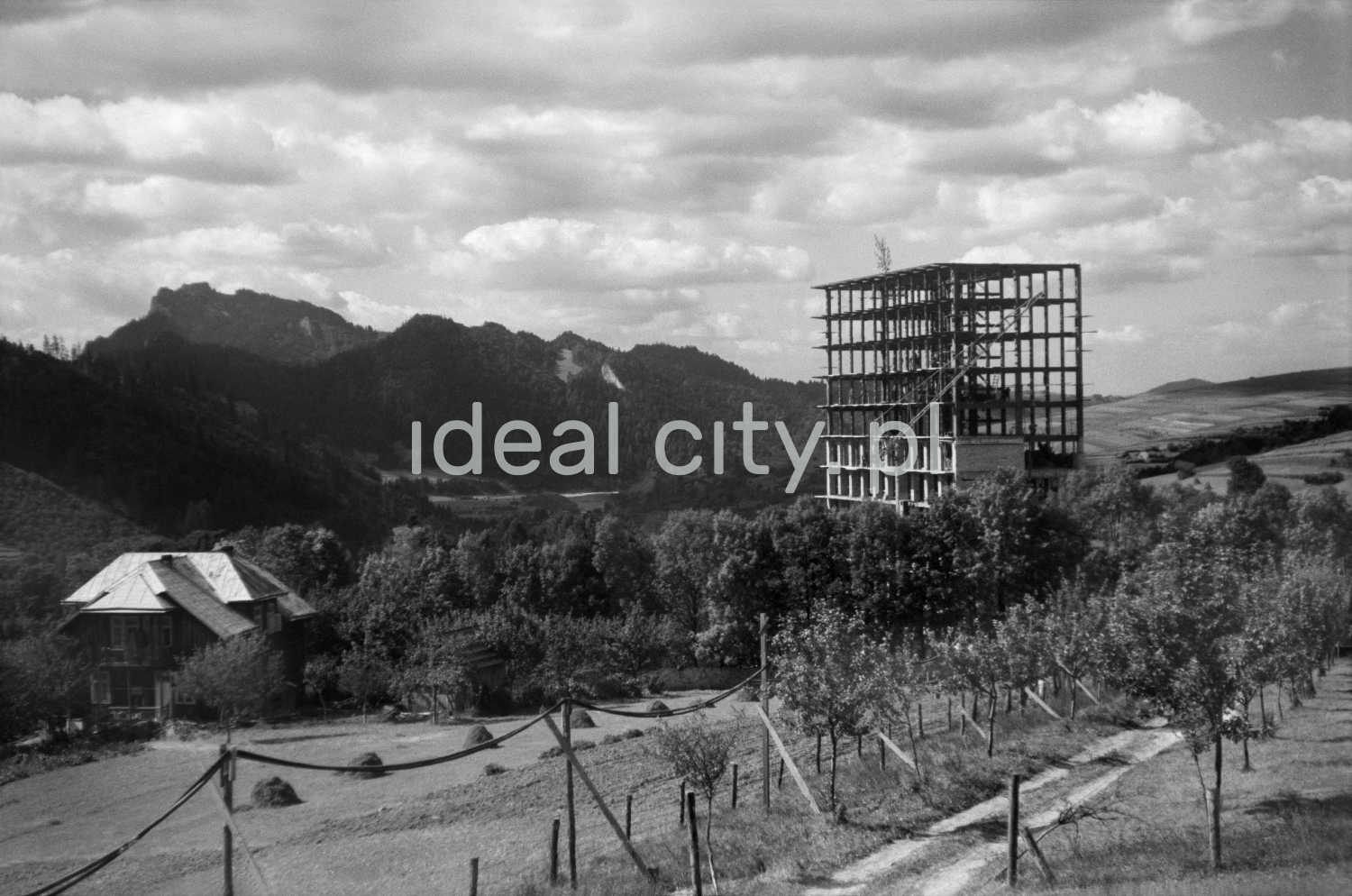 A view of the reinforced concrete skeleton of a modernist building, top floor with a panicle and mountain peaks in the background.