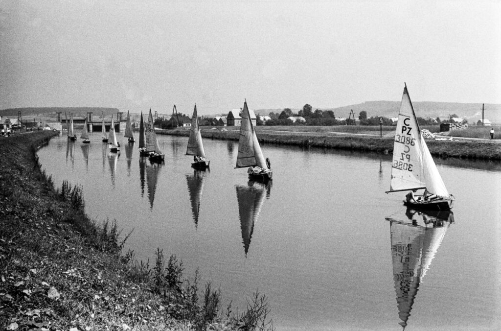 Sailboats follow the river in a row, one after the other.
