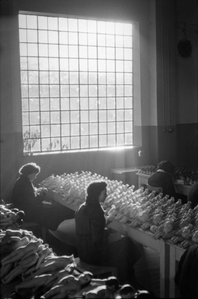 Women workers assembling doll's bodies inside production hall.