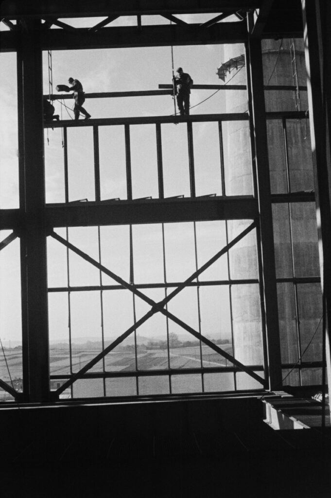 Workers on the openwork wall structure of a factory hall under construction.