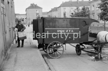 Pocztowy wóz konny do przewożenia paczek i listów przed budynkiem pierwszej poczty w Nowej Hucie na osiedlu A-1 Północ (Willowe). Została ona otwarta w połowie 1951 roku. Wystrój wnętrza, m.in. meble, kolumny pokryte marmurową okładziną, marmurowe blaty, zaprojektował Marian Sigmund. Pierwotnie w tym budynku (na piętrze) miał swoją siedzibę również Międzyzwiązkowy Klub Robotniczy. Na parterze znajdowały się punkty przyjęcia klientów, a na piętrze m.in. rozdzielnia oraz mieszkanie służbowe listonosza, który był jednocześnie stróżem. Listonosze dzielili się na miejskich i wiejskich, norma listonosza miejskiego wynosiła 2 tysiące mieszkańców. Na początku pracowało 7 listonoszy. W tle widoczne domy mieszkalne według projektów warszawskiego architekta Franciszka Adamskiego. Lata 50/60. XXw.

fot. Wiktor Pental/idealcity.pl

