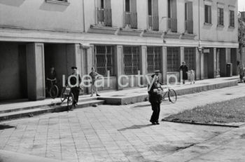 Listonosze wyprowadzający rowery z budynku poczty na osiedlu A-1 Północ (Willowe). Poczta została otwarta w połowie 1951 roku. Wystrój wnętrza, m.in. meble, kolumny pokryte marmurową okładziną, marmurowe blaty, zaprojektował Marian Sigmund. Pierwotnie w tym budynku (na piętrze) miał swoją siedzibę również Międzyzwiązkowy Klub Robotniczy. Na parterze znajdowały się punkty przyjęcia klientów, a na piętrze m.in. rozdzielnia oraz mieszkanie służbowe listonosza, który był jednocześnie stróżem. Listonosze dzielili się na miejskich i wiejskich, norma listonosza miejskiego wynosiła 2 tysiące mieszkańców. Na początku pracowało 7 listonoszy. W tle widoczne domy mieszkalne według projektów warszawskiego architekta Franciszka Adamskiego. Koniec lat 50. XXw.

fot. Wiktor Pental/idealcity.pl

