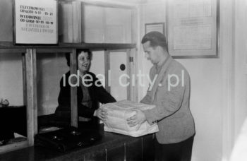 Wnętrze pierwszego urzędu pocztowego w Nowej Hucie, na osiedlu A-1 Północ (Willowe). Poczta została otwarta w połowie 1951 roku. Wystrój wnętrza, m.in. meble, kolumny pokryte marmurową okładziną, marmurowe blaty, zaprojektował Marian Sigmund. Pierwotnie w tym budynku (na piętrze) miał swoją siedzibę również Międzyzwiązkowy Klub Robotniczy. Na parterze znajdowały się punkty przyjęcia klientów, a na piętrze m.in. rozdzielnia oraz mieszkanie służbowe listonosza, który był jednocześnie stróżem. Listonosze dzielili się na miejskich i wiejskich, norma listonosza miejskiego wynosiła 2 tysiące mieszkańców. Na początku pracowało 7 listonoszy. W tle widoczne domy mieszkalne według projektów warszawskiego architekta Franciszka Adamskiego. Koniec lat 50. XXw. 

fot. Wiktor Pental/idealcity.pl


